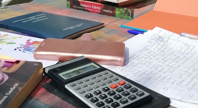 The desk of a researcher with mobile phone, books, papers and vintage calculator.